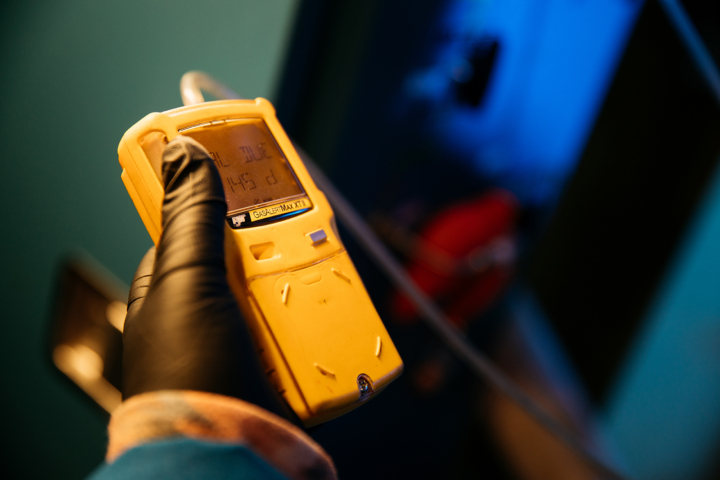 A gloved hand holding a gas tester with an electronic display