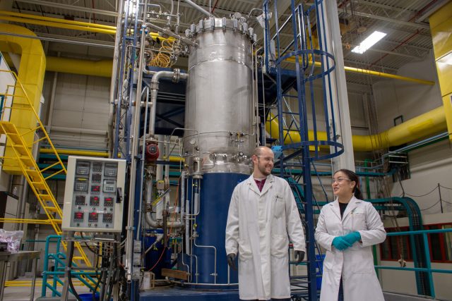 Two researchers standing in from of a fermentation plant
