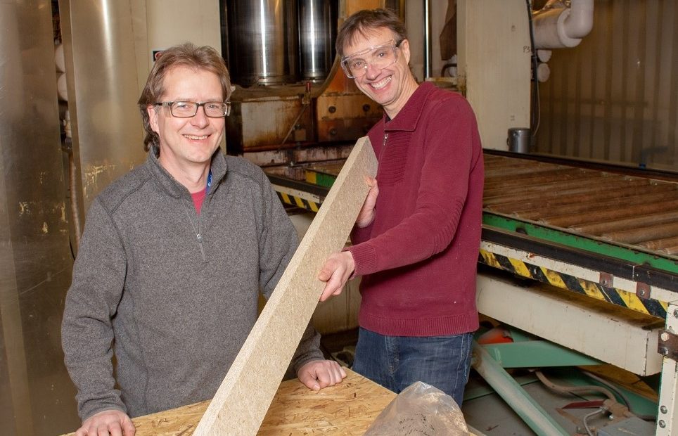 Two men posing with a piece of lumber