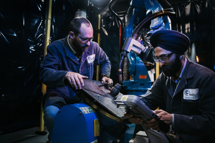 Two men working with a robotic welder
