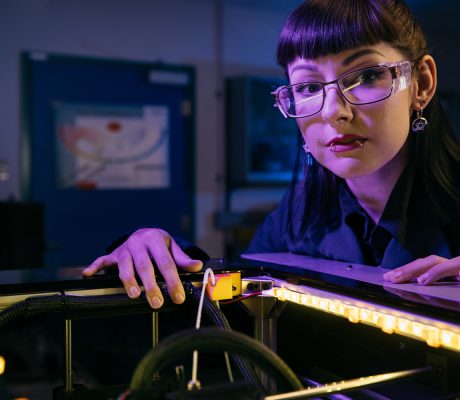 Dark-haired woman with glasses leaning over a 3D printer
