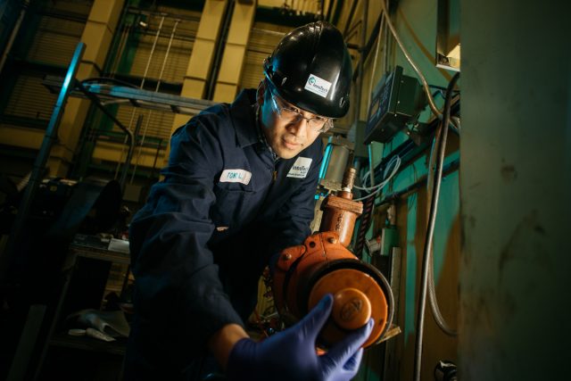 InnoTech researcher wearing a hard hat and tightening a valve