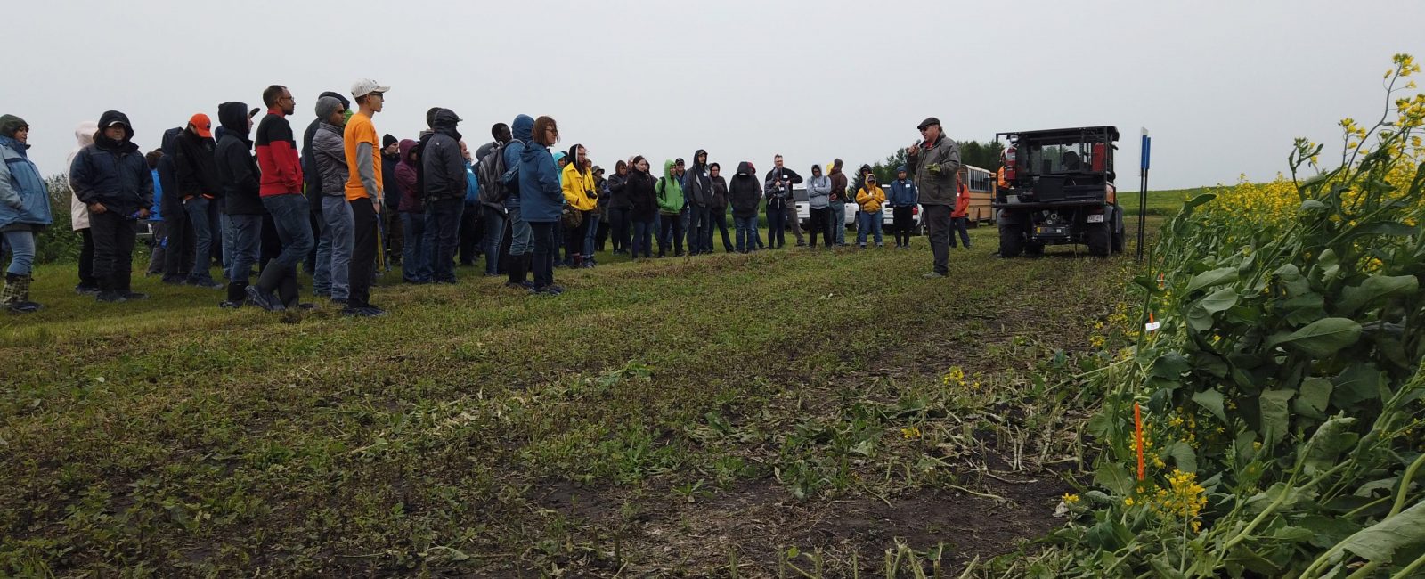 A group of people standing in a field listening to a speaker