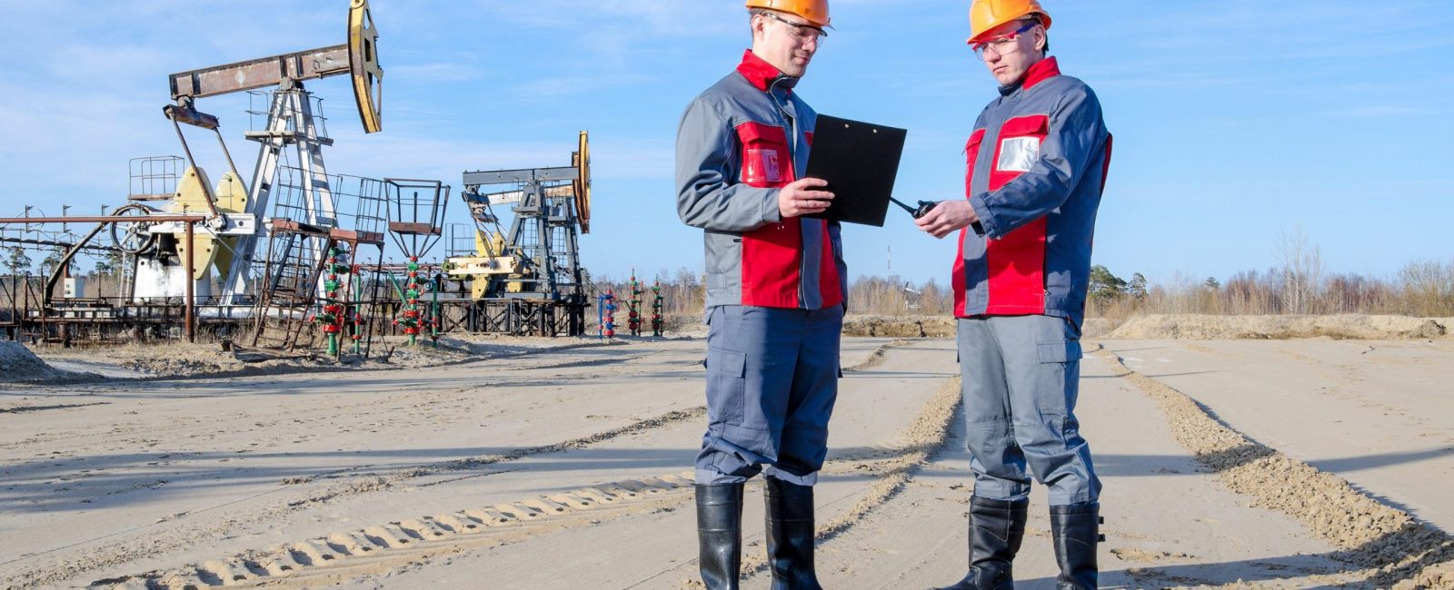 Two workers discussing plans amid the oilfield.